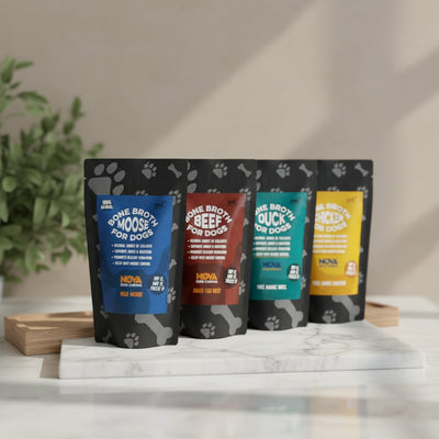 Three packages of Nova Bone Broth for Dogs in different flavors (Moose, Duck, Beef) displayed on a wooden surface with a paw print pattern. Each pack has a label indicating it's a free range bone broth, organic, and suitable for dogs.