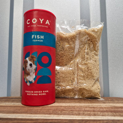Red COYA fish topper canister and bag of pet food on a wooden surface with a striped wall background.