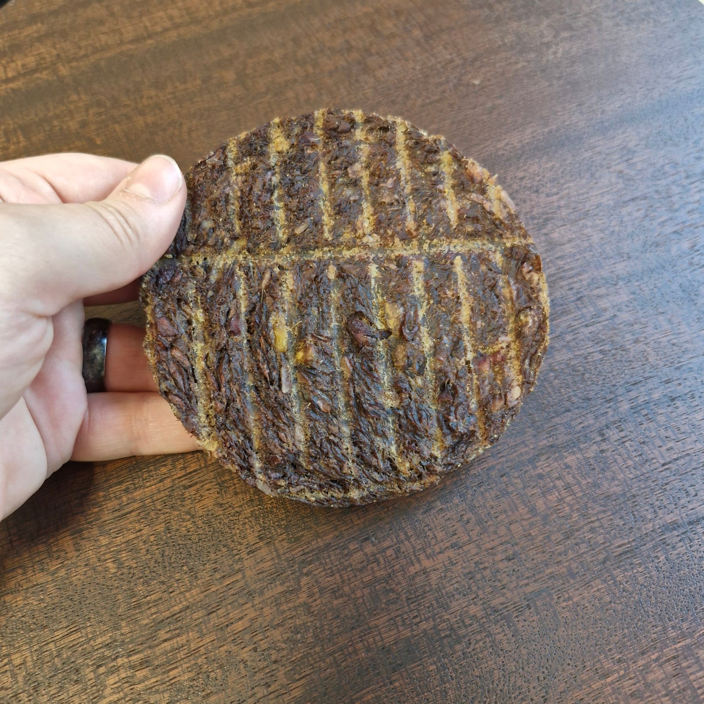 Hand holding a round, dark brown object with grid pattern on a wooden surface